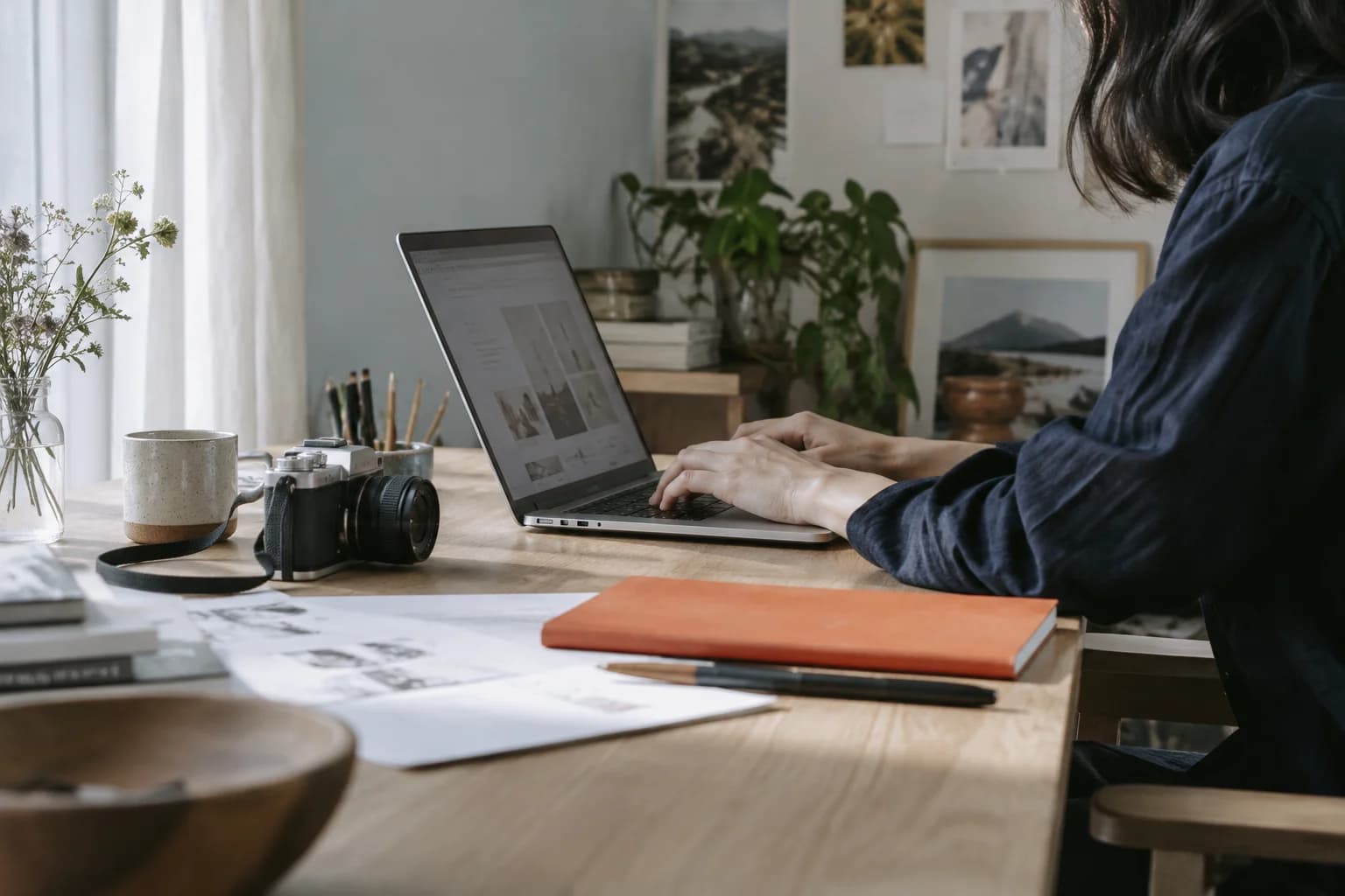 A creator working at a desk with a camera, notebook, and laptop.
